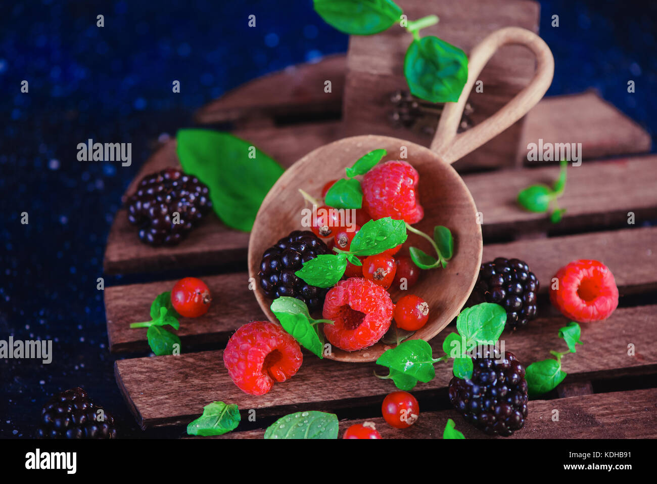 Frutti di bosco assortiti in una serva piatto di legno. lampone e blackberry con verde menta foglie scure della fotografia di cibo con copia spazio. Foto Stock