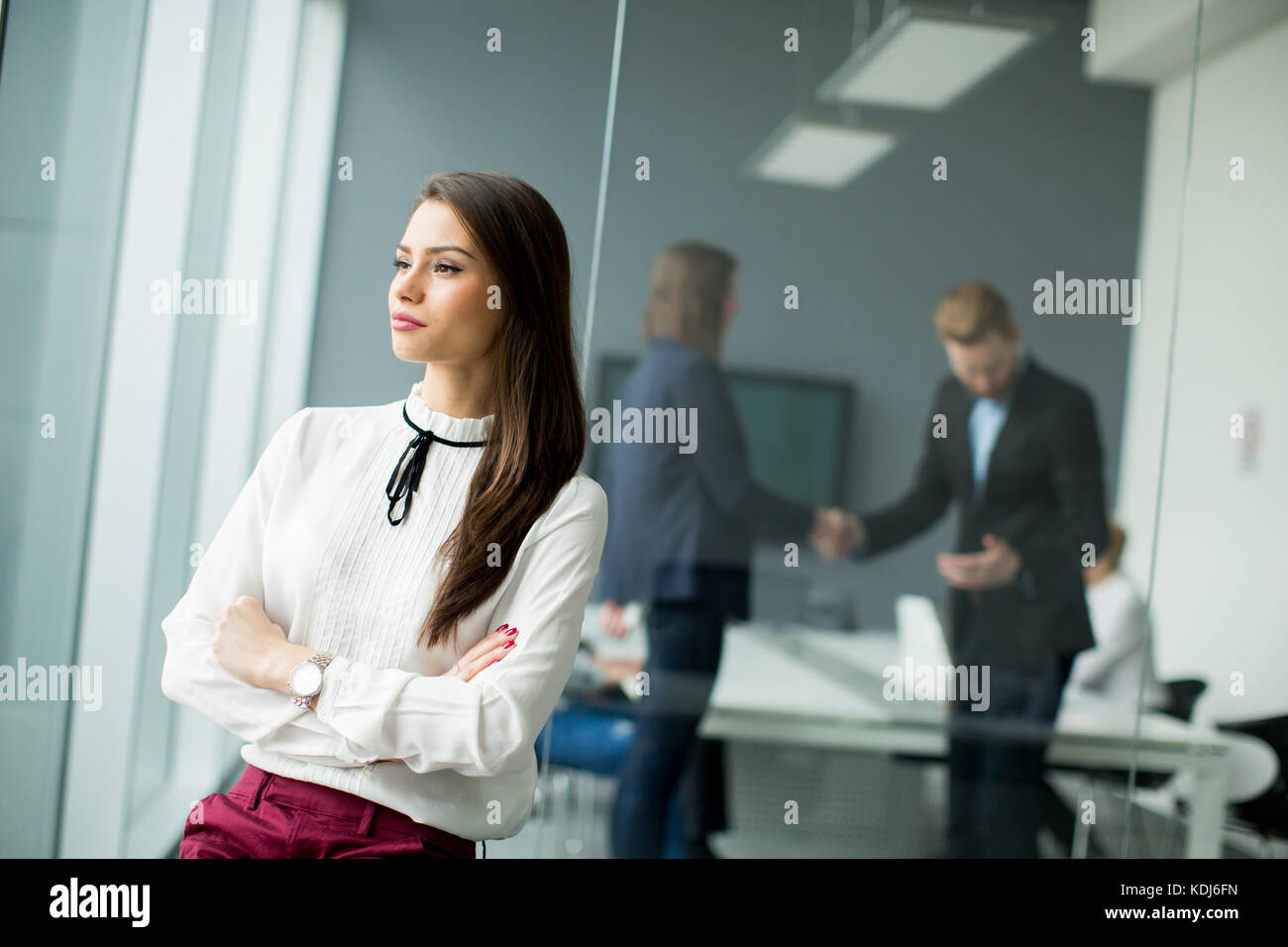 Giovane imprenditrice in piedi in un ufficio moderno con giovani uomini di affari in background che seduta Foto Stock