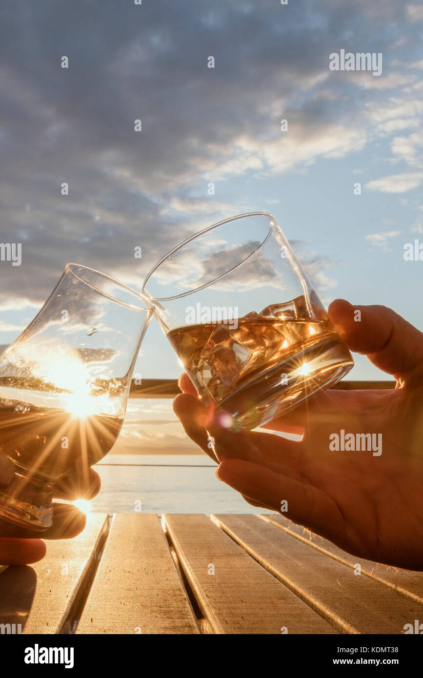 Angolo basso vicino fino a due mani la tostatura le bevande alcoliche al di fuori sul ponte al tramonto ritratto. Foto Stock