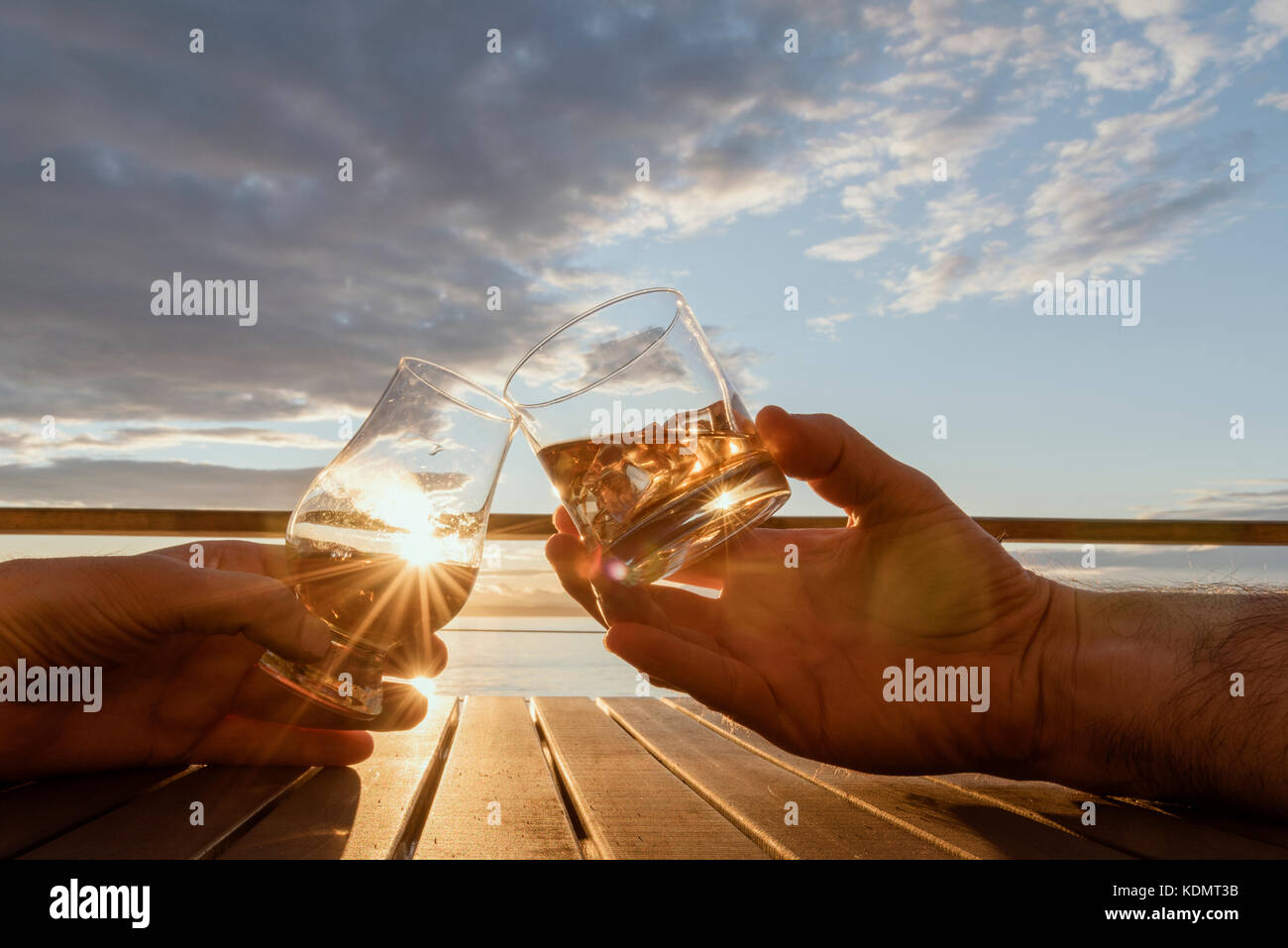 Angolo basso vicino fino a due mani la tostatura le bevande alcoliche al di fuori sul ponte al tramonto paesaggio orizzontale. Foto Stock