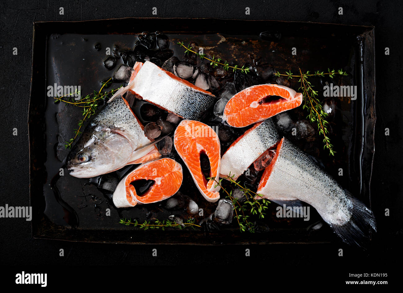 Crudo fresco pezzi di salmone pesce rosso con ghiaccio su uno sfondo scuro. flat laici. vista superiore Foto Stock