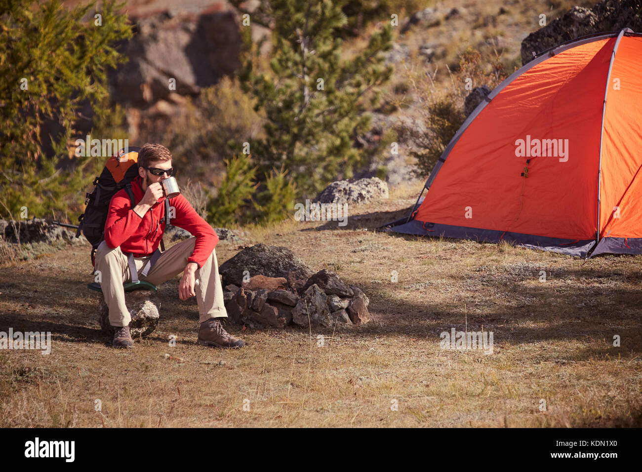 Backpacker avente resto vicino a Orange tenda, bevande di tè da cup . Foto Stock