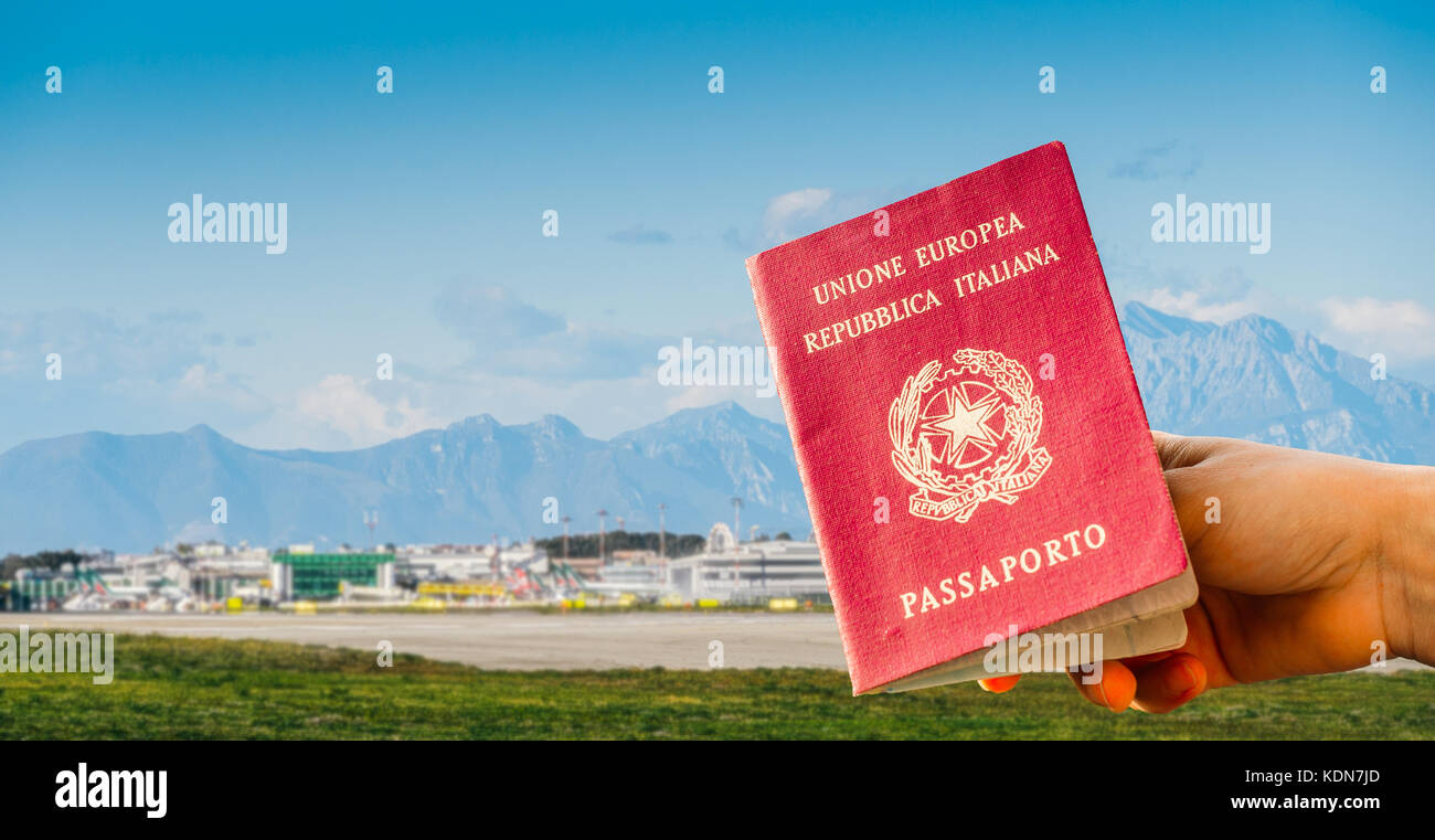 Composito Digitale di mano in possesso di un passaporto italiano con trafficato terminal dell'aeroporto vicino alle montagne in sfondo sfocato Foto Stock