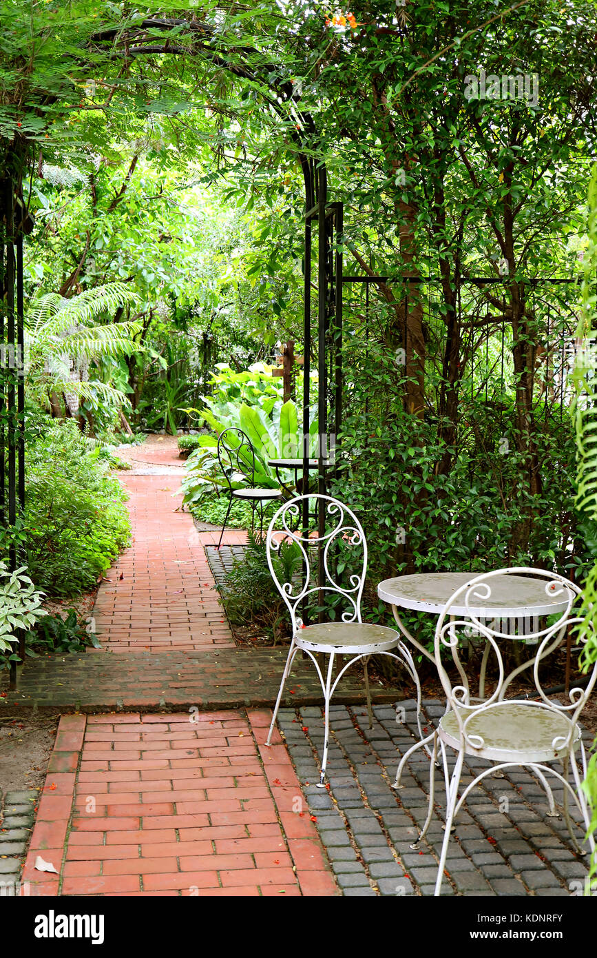 Foto verticale bianca di letti in ferro battuto con tavolo e sedie nel giardino con mattoni tratto lastricato Foto Stock