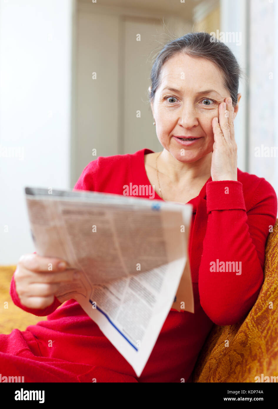 Chiedo dolore donna con giornale sul divano di casa Foto Stock