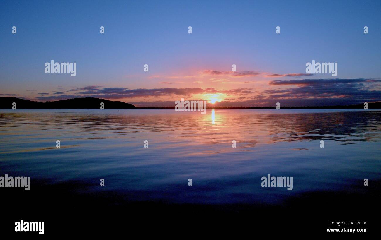 Oro e grigio alba mare con riflessi d'acqua nelle acque tranquille del lago Macquarie all'alba. Nuovo Galles del Sud, Australia. Foto Stock
