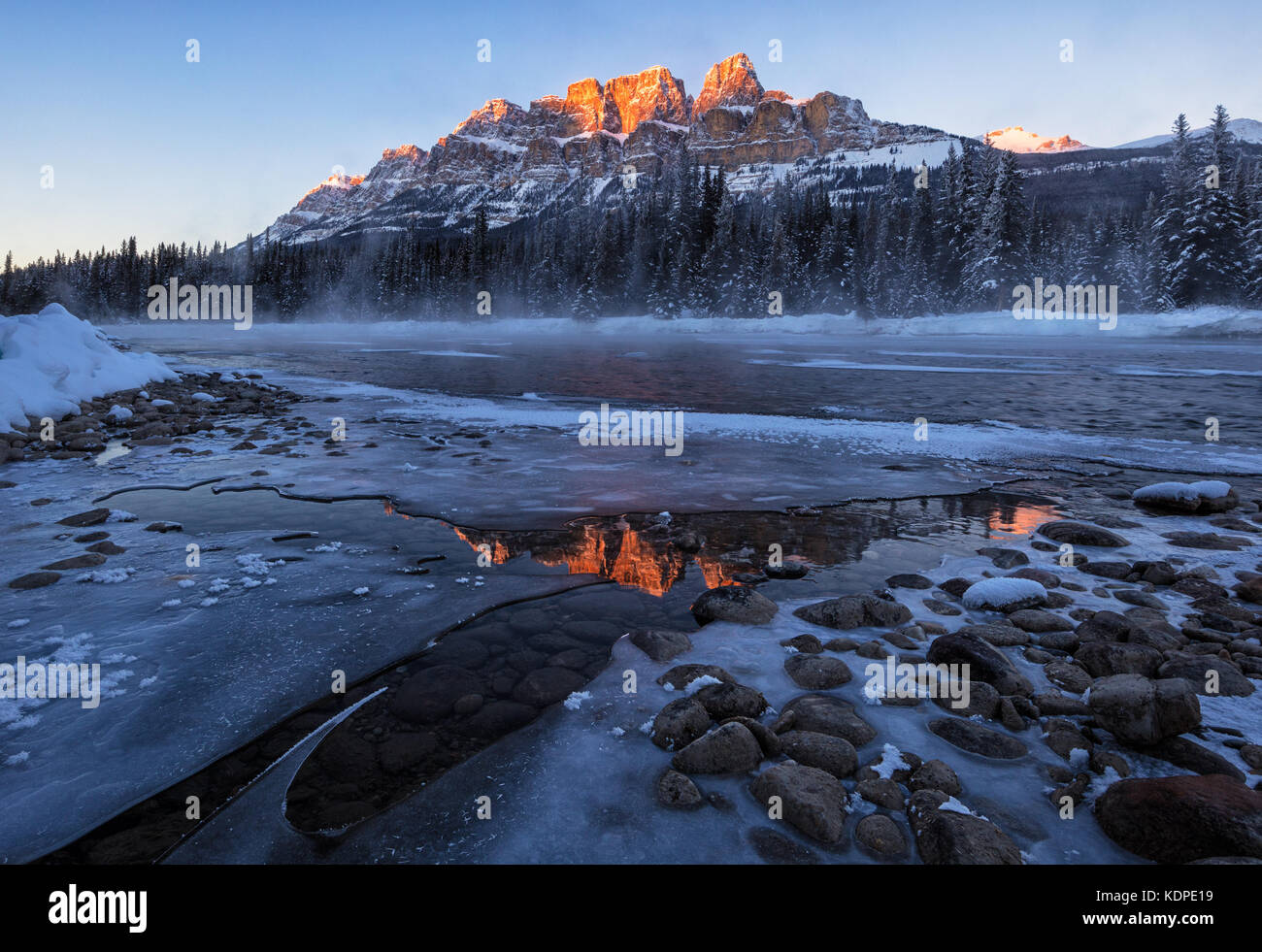 Tramonto in inverno al castello di montagna, il parco nazionale di Banff a -27 gradi celsius con chiaro riflesso nell'acqua ghiacciata e nebbioso fiume bow. Foto Stock