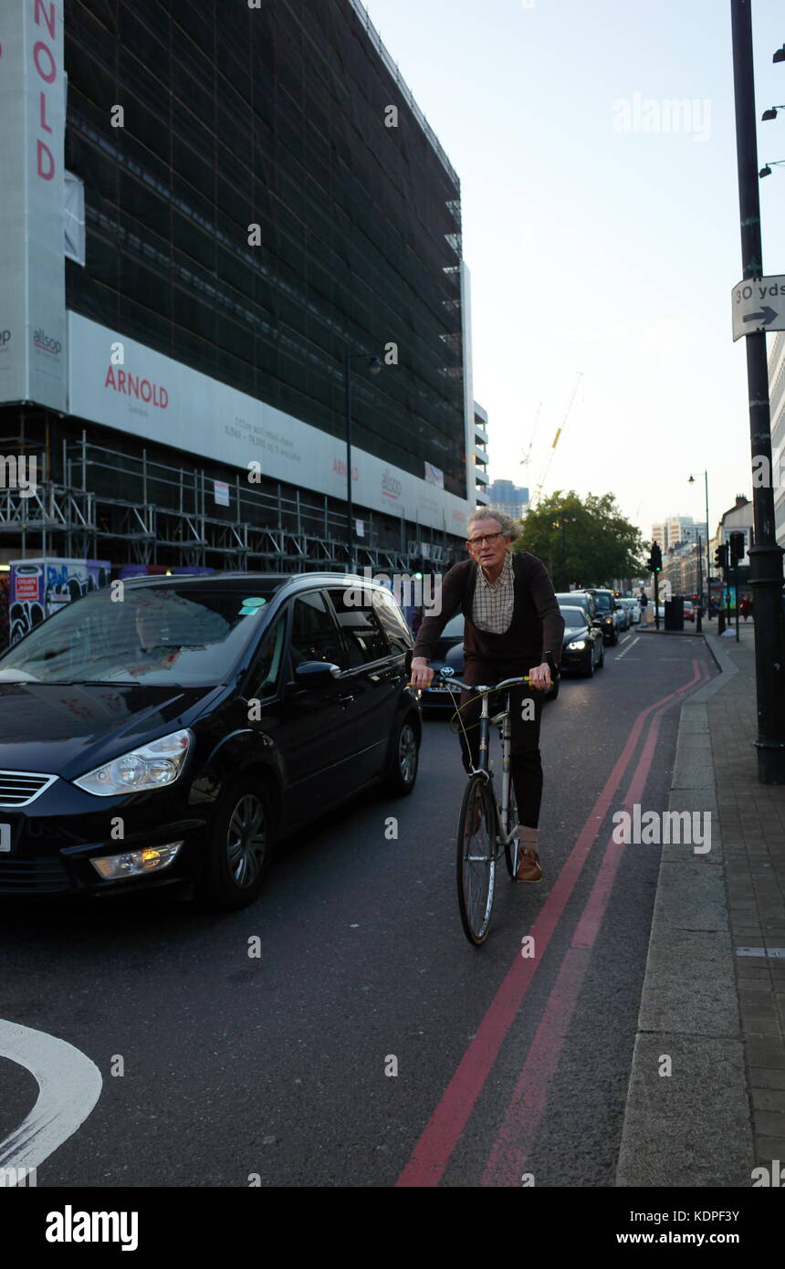 Uomo che guarda come un mad professor pedalando attraverso il traffico di veicoli a Londra in Inghilterra Foto Stock