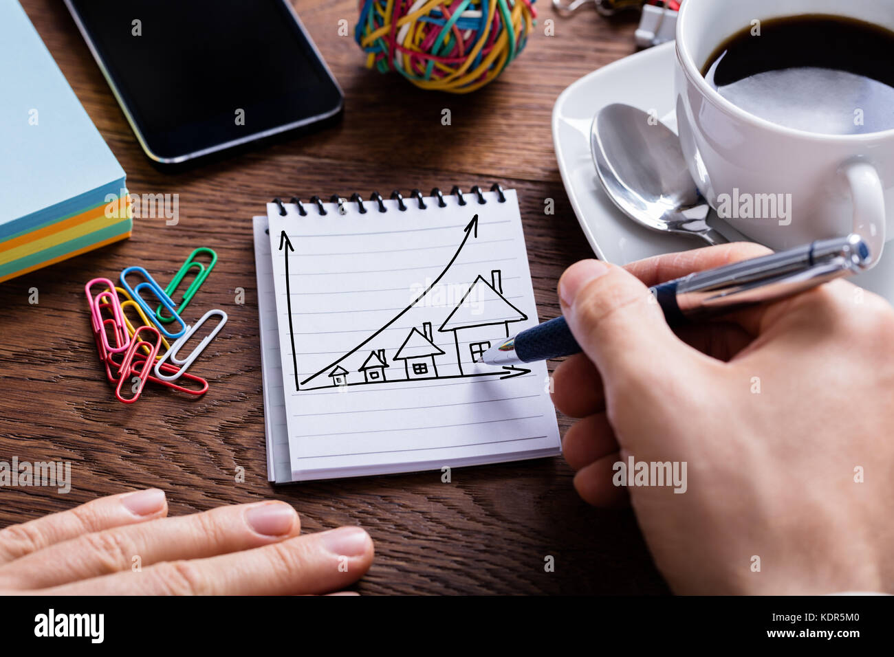 Elevato angolo di visione della persona disegno casa prezzi il concetto di crescita su blocco note Foto Stock