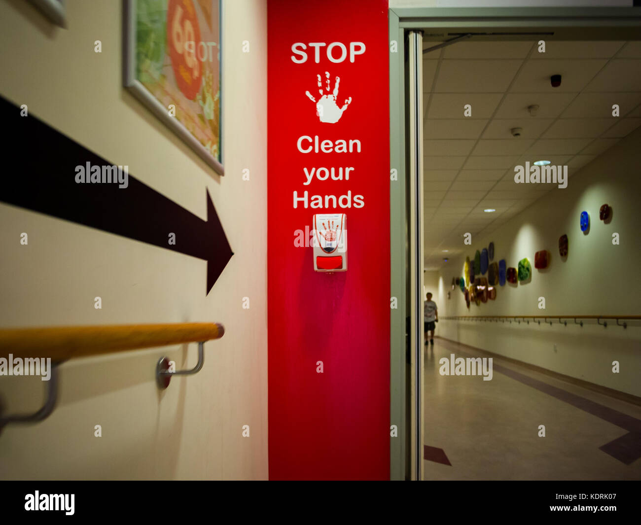 Un alcool gel stazione di erogazione per la disinfezione delle mani all'interno di un ospedale con un segnale di avvertimento. Foto Stock