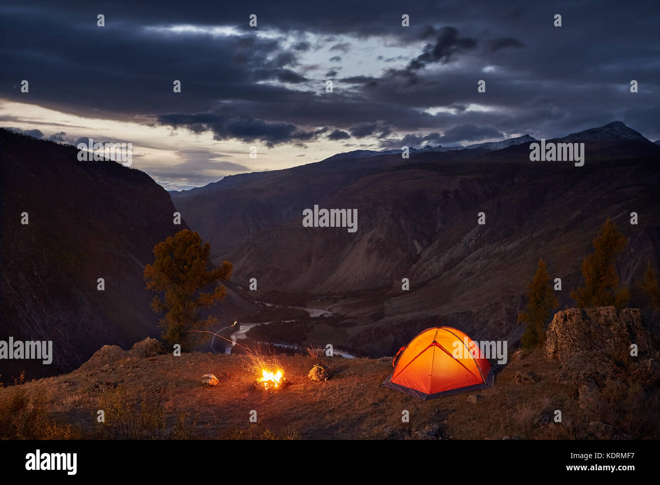 Una tenda illuminata e falò in montagna in Alba Foto Stock