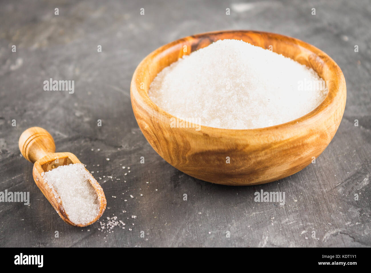 Zucchero bianco zucchero in un piatto di legno con una paletta su uno sfondo scuro. Foto Stock