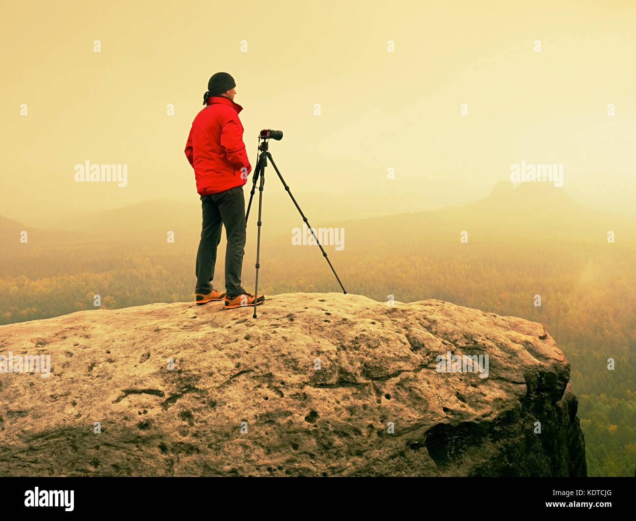 Fotografo professionista sulla posizione di scattare foto con la fotocamera dello specchietto sul picco di roccia. dreamy foggy paesaggio, primavera rosa arancione misty sunrise in b Foto Stock