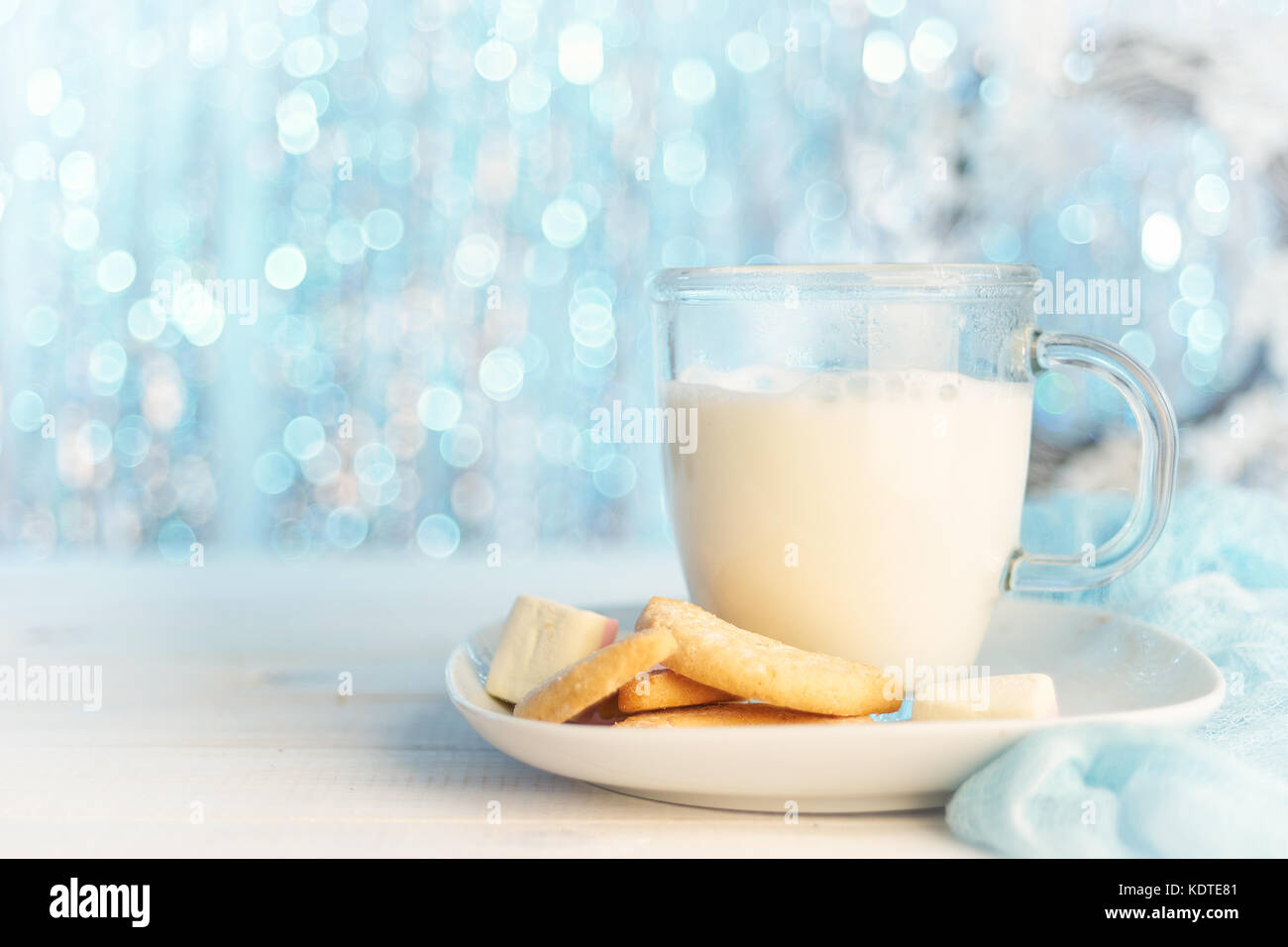 Tazza di vetro di latte caldo con i cookie su luce glitter sfondo per natale. copia spazio. Foto Stock