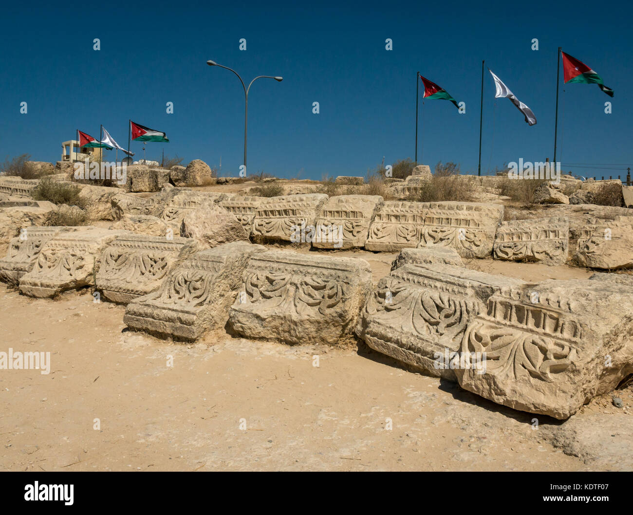 Intagliato topping rovina le pietre esposte nella città romana di Jerash, antica Gerasa, sito archeologico, Giordania, Medio Oriente con bandiere giordane Foto Stock