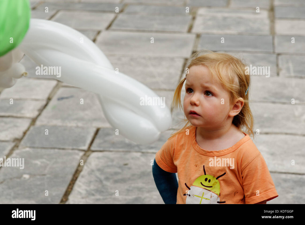 Una bambina di 3 anni a guardare un palloncino scultore rendendo un palloncino Foto Stock