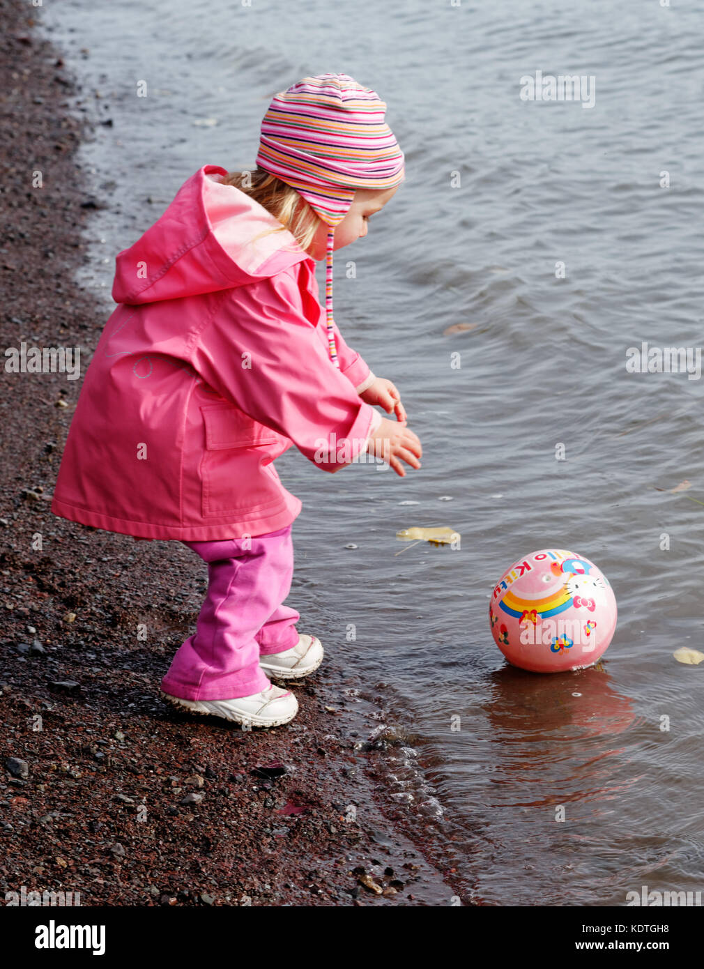 Una bambina di 3 anni nel tentativo di raggiungere la sua palla che ha rotolato nel mare Foto Stock