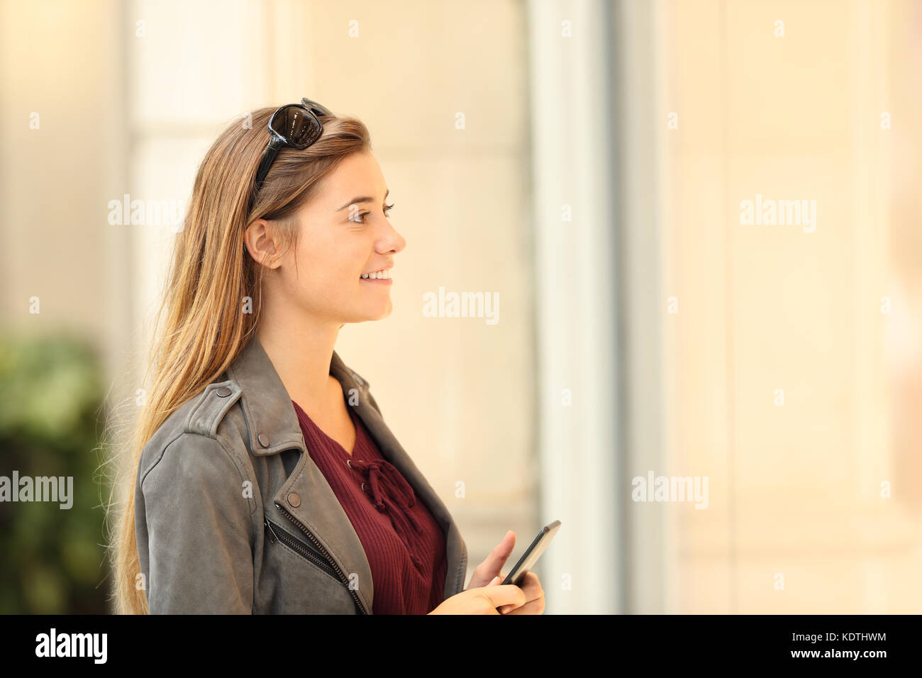 Vista laterale di un felice shopper guardando una vetrina in possesso di una smart phone all'aperto sulla strada Foto Stock