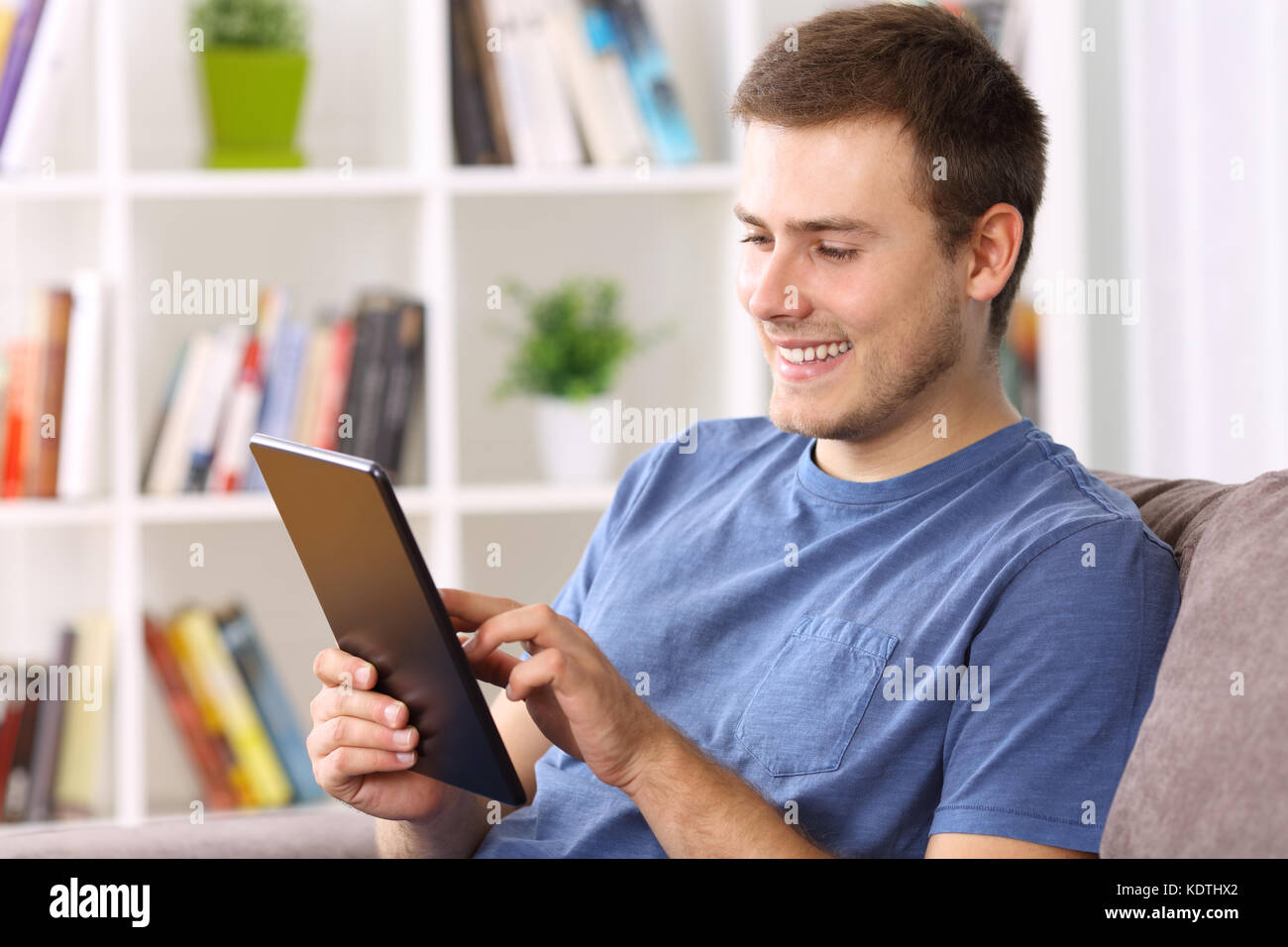 Felice l'uomo utilizzando un tablet seduto su un divano a casa Foto Stock