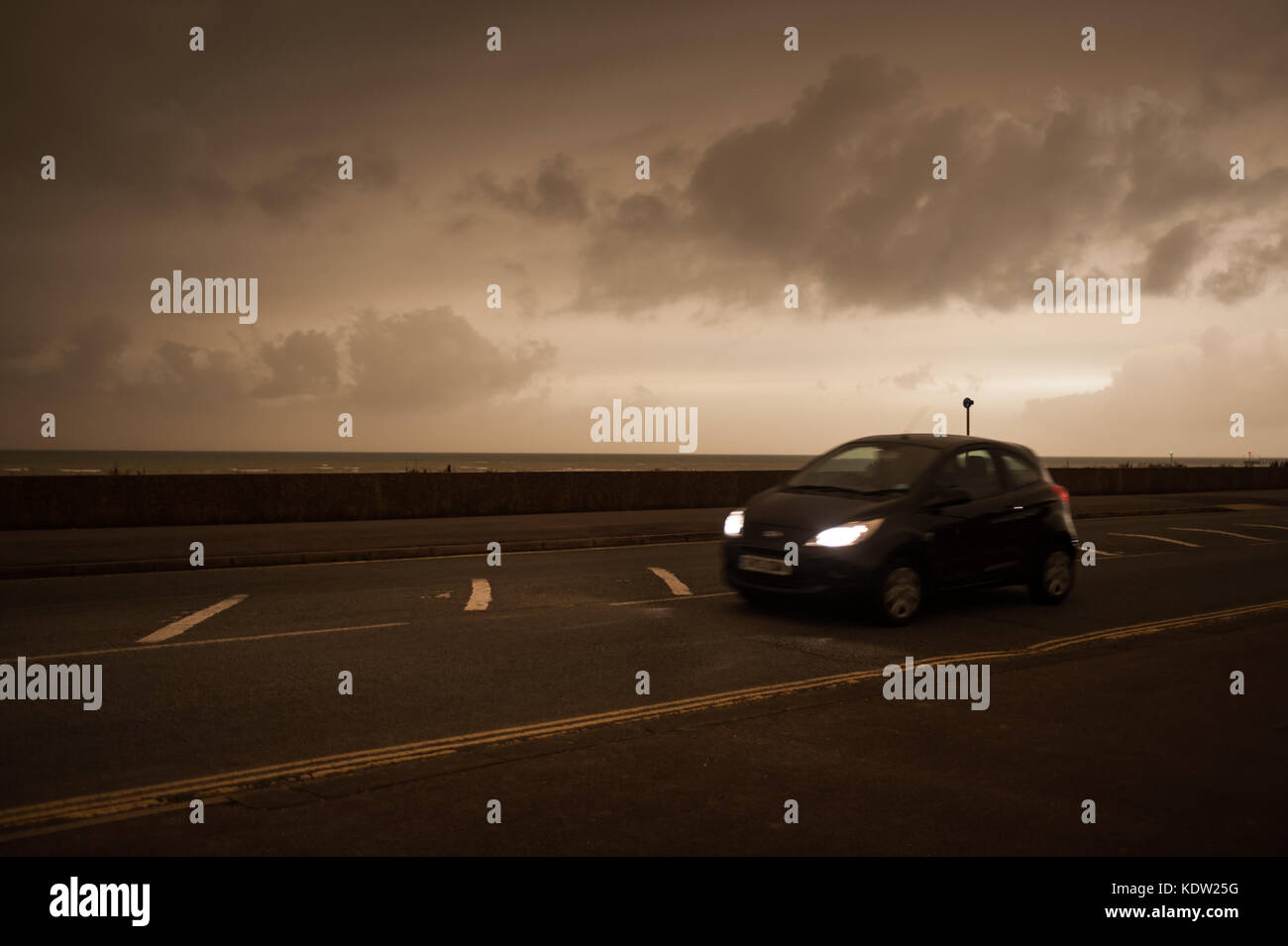 Il giorno si trasforma in notte come una unità auto lungo il lungomare di Littlehampton West Sussex, in Inghilterra. Il cielo si è oscurato e uno strano bagliore arancione è apparso nel bel mezzo della giornata. Le luci di strada è venuto su e i piloti hanno dovuto mettere i loro fari su. Rapporti dire il fenomeno è stato causato dalla ex uragano, Storm Ofelia, tirando in aria e polvere dall'Europa meridionale e in Africa. Foto Stock