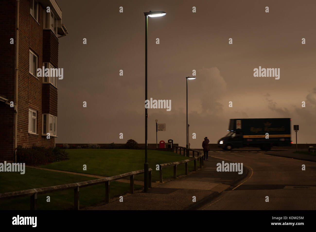 Il giorno si trasforma in notte come una donna cammina lungo un tratto di strada in Littlehampton West Sussex, in Inghilterra. Il cielo si è oscurato e uno strano bagliore arancione è apparso nel bel mezzo della giornata. Le luci di strada è venuto su e i piloti hanno dovuto mettere i loro fari su. Rapporti dire il fenomeno è stato causato dalla ex uragano, Storm Ofelia, tirando in aria e polvere dall'Europa meridionale e in Africa. Foto Stock