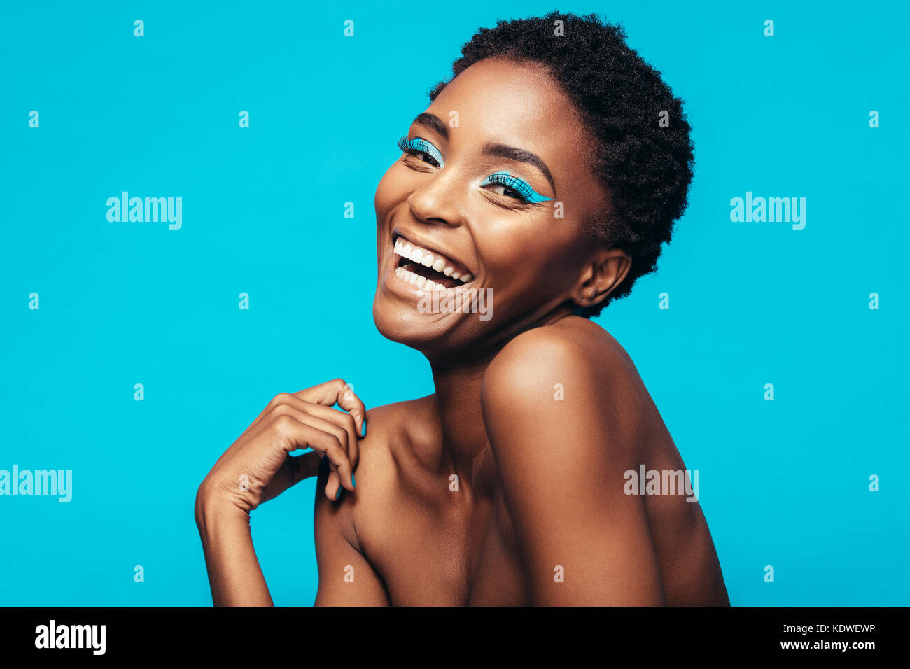 Close up allegro giovane donna con vivaci trucco su i suoi occhi. African modello femminile di ridere contro lo sfondo blu. Foto Stock