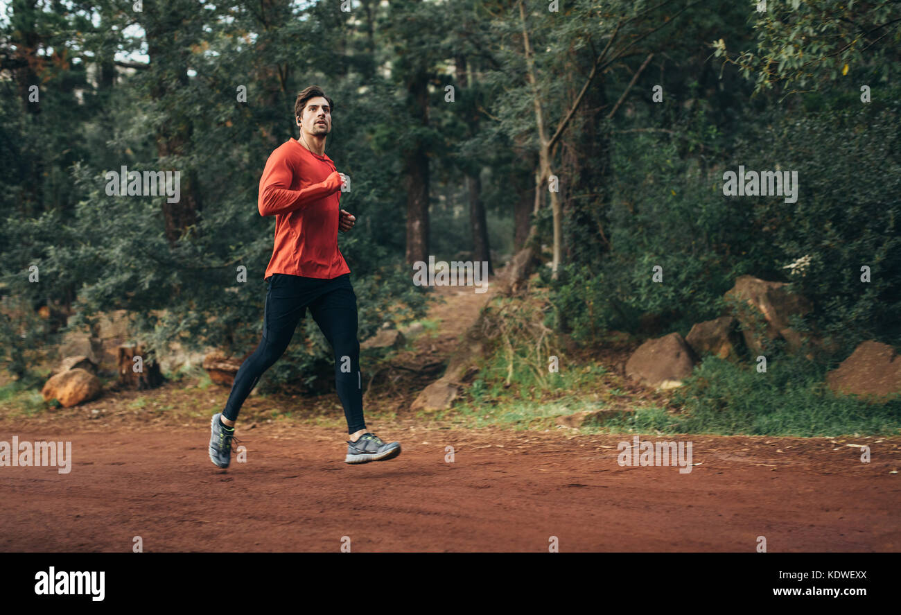 Runner in articoli sportivi jogging in un parco. Uomo che corre su terreni fangosi park trail. Foto Stock