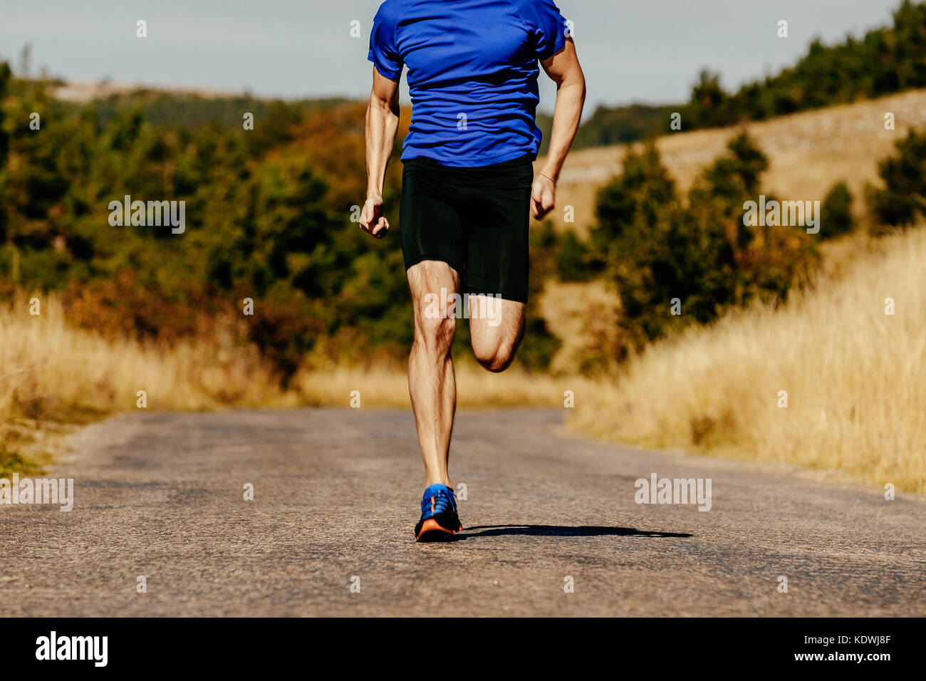 Gambe muscolare uomini runner in esecuzione su strada asfaltata in campo di autunno Foto Stock