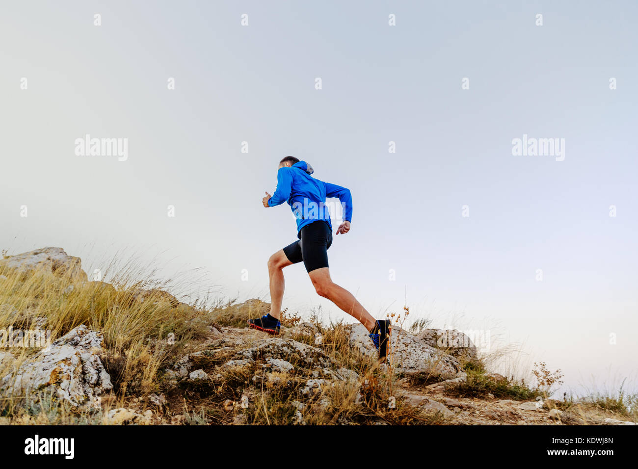 In esecuzione in salita su pietre atleta maschio runner vista laterale Foto Stock