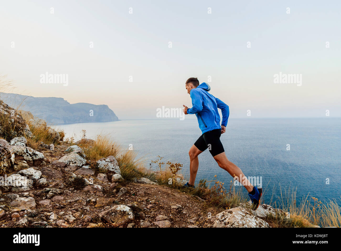In esecuzione in salita nel sentiero atleta maschio runner su sfondo del mare Foto Stock