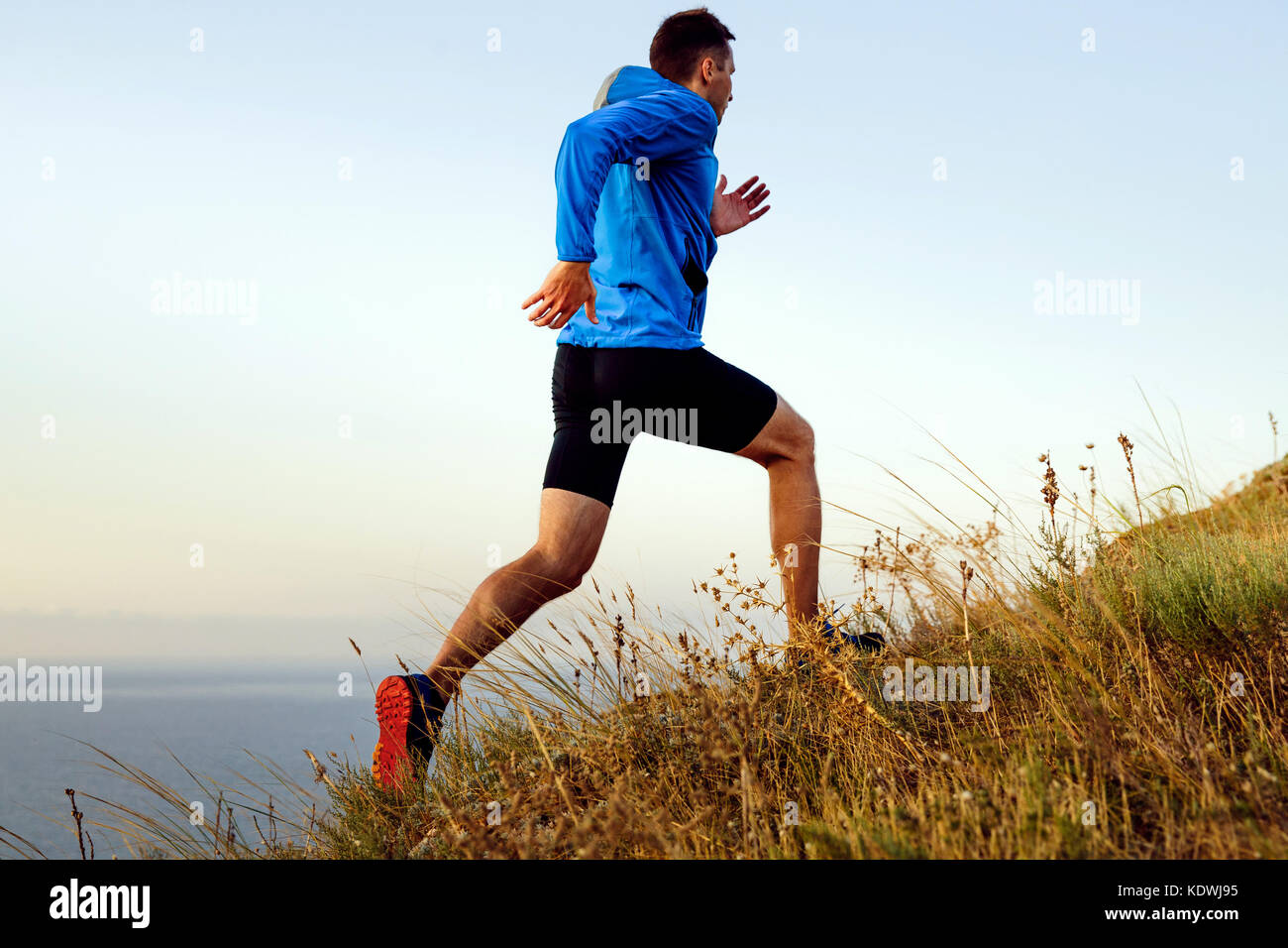 Esecuzione dinamica in salita atleta maschio runner sullo sfondo del mare e del cielo Foto Stock
