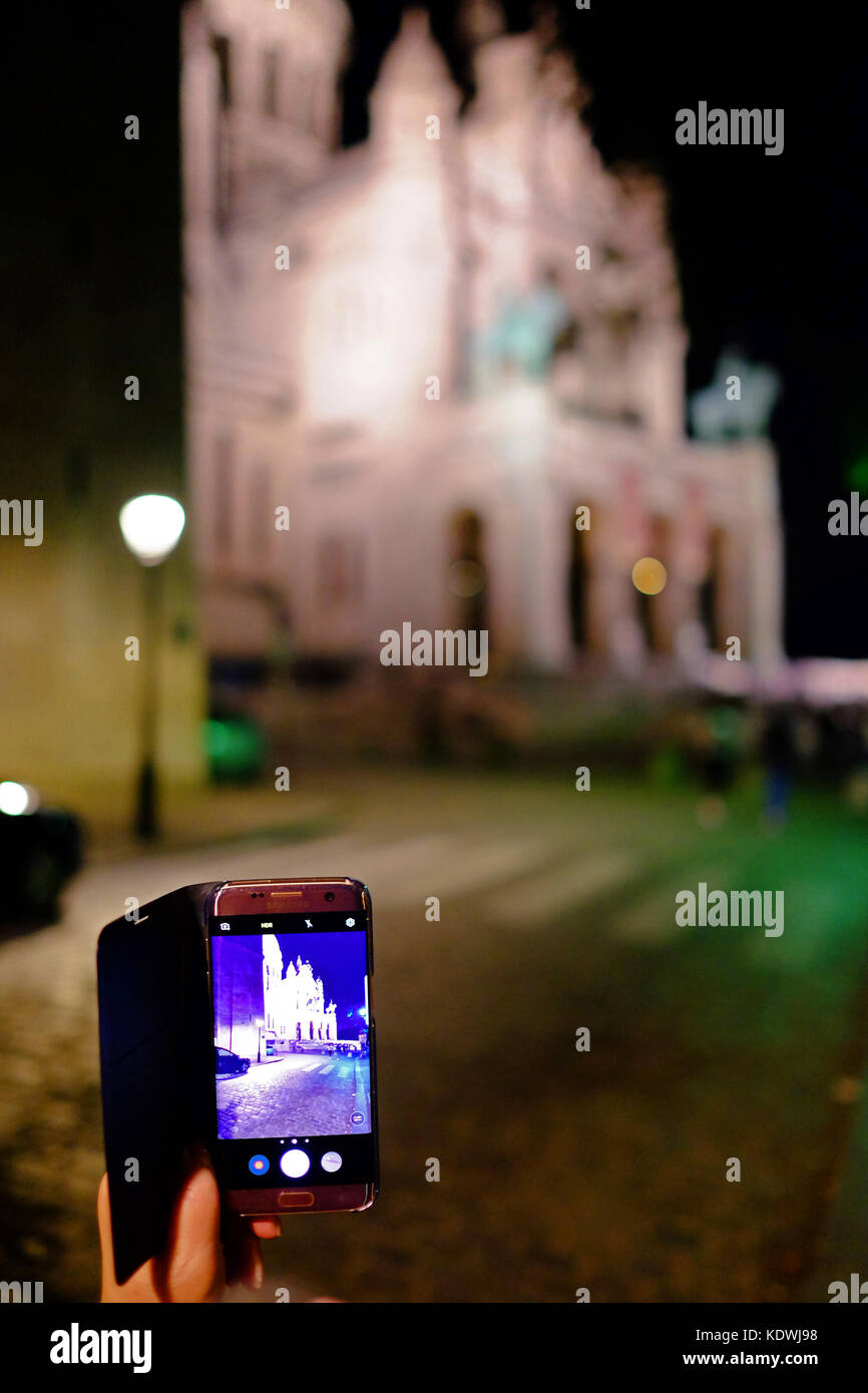 Un turista di scattare una foto sul suo smartphone Samsung del Sacre Coeur in Motmartre, Parigi di notte Foto Stock