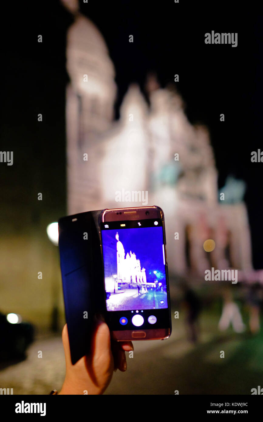 Un turista di scattare una foto sul suo smartphone Samsung del Sacre Coeur in Motmartre, Parigi di notte Foto Stock