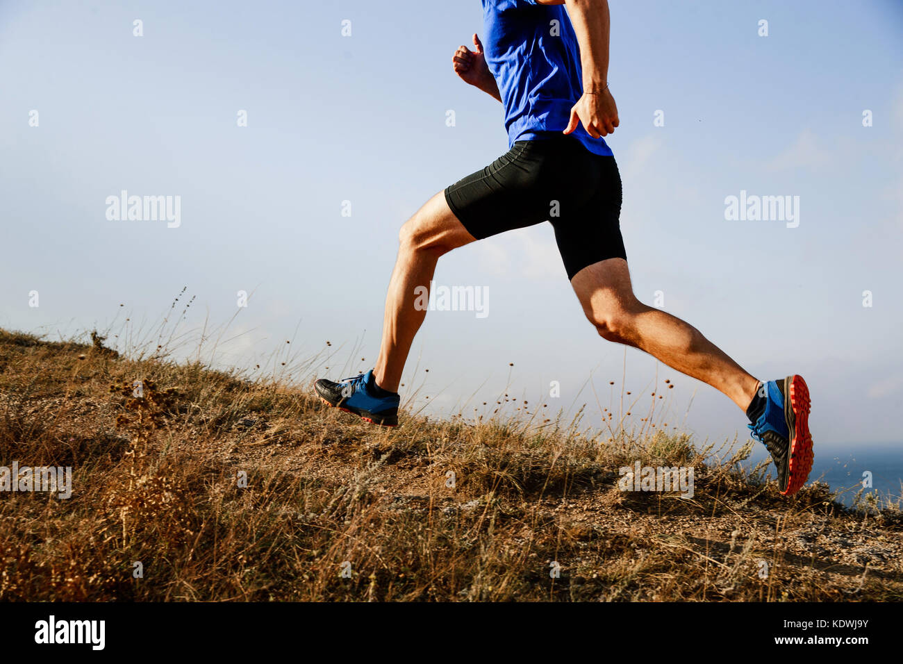 Gambe atleta maschio runner acceso in salita su sentiero sullo sfondo di un cielo Foto Stock