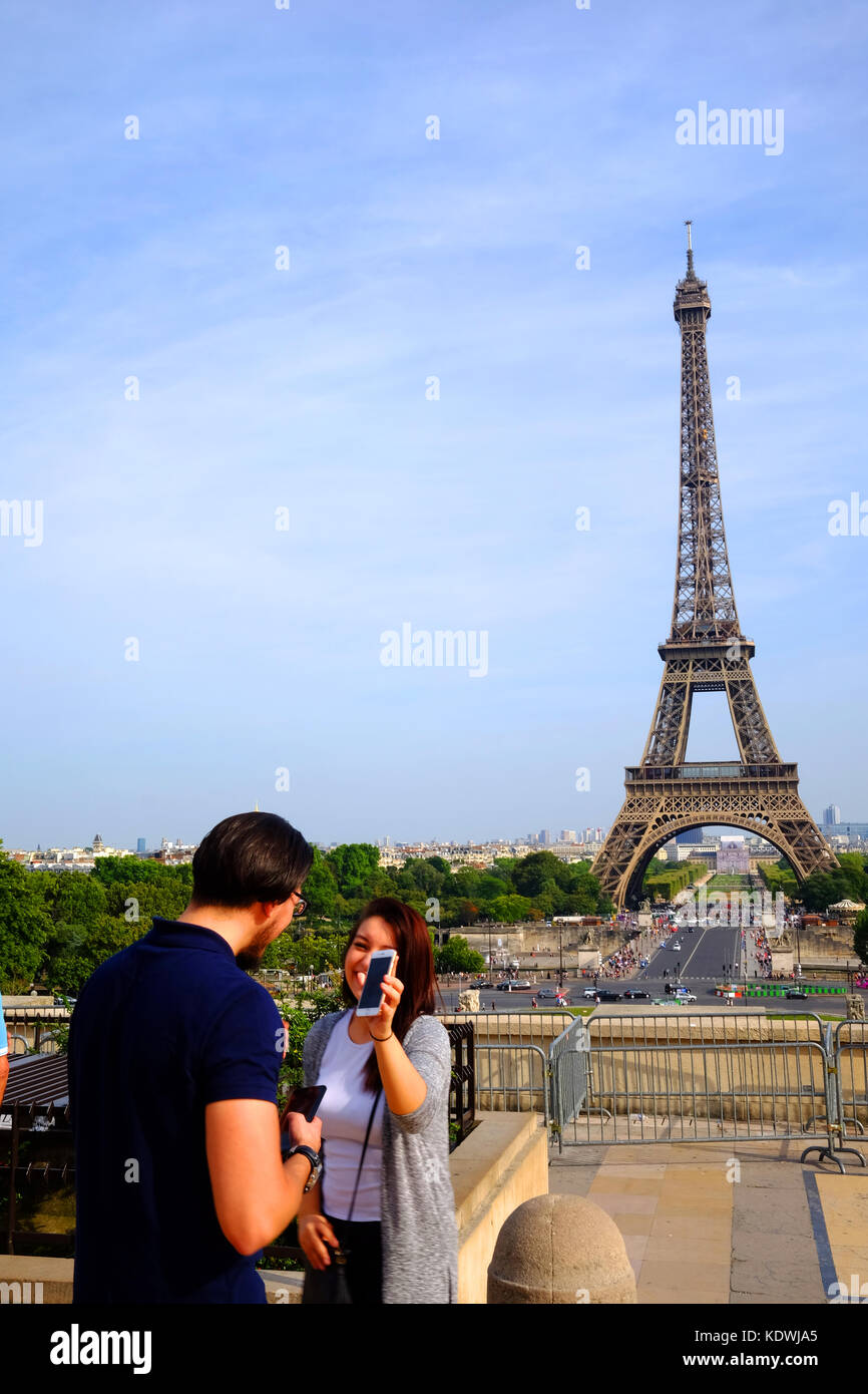 Una giovane coppia che mostra ogni altro il selfies hanno preso sui loro smartphone con la Torre Eiffel a Parigi in background Foto Stock