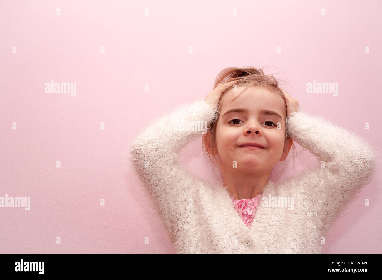 Di piccole dimensioni e di colore bianco caucasico ragazza bionda bambino le mani sulla testa tirando hari pianura sfondo rosa Foto Stock