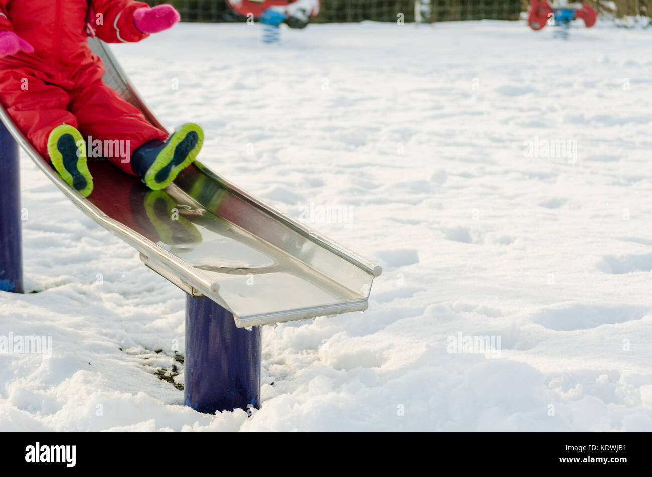 Kid giocare all'aperto nella neve. Inverno attivo stile di vita. Preschooler bambino su una diapositiva in un parco giochi con motion blur Foto Stock
