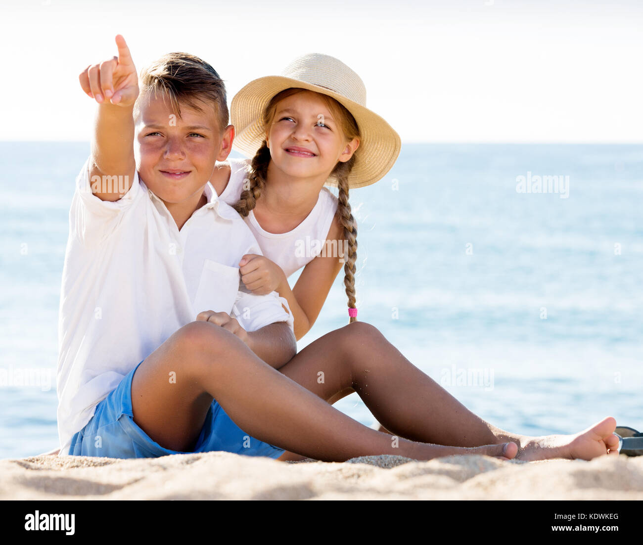 Felice un ragazzo e una ragazza puntando con il dito sulla spiaggia di sabbia sulla luminosa meteo Foto Stock