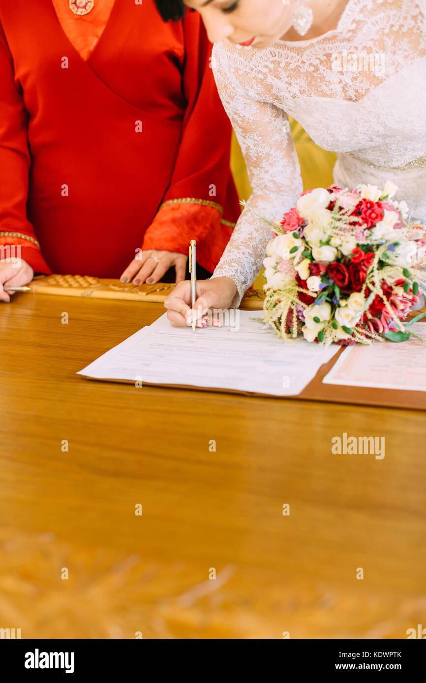 Vista ravvicinata della sposa di firmare il documento di matrimonio mentre si tiene il bouquet. Foto Stock