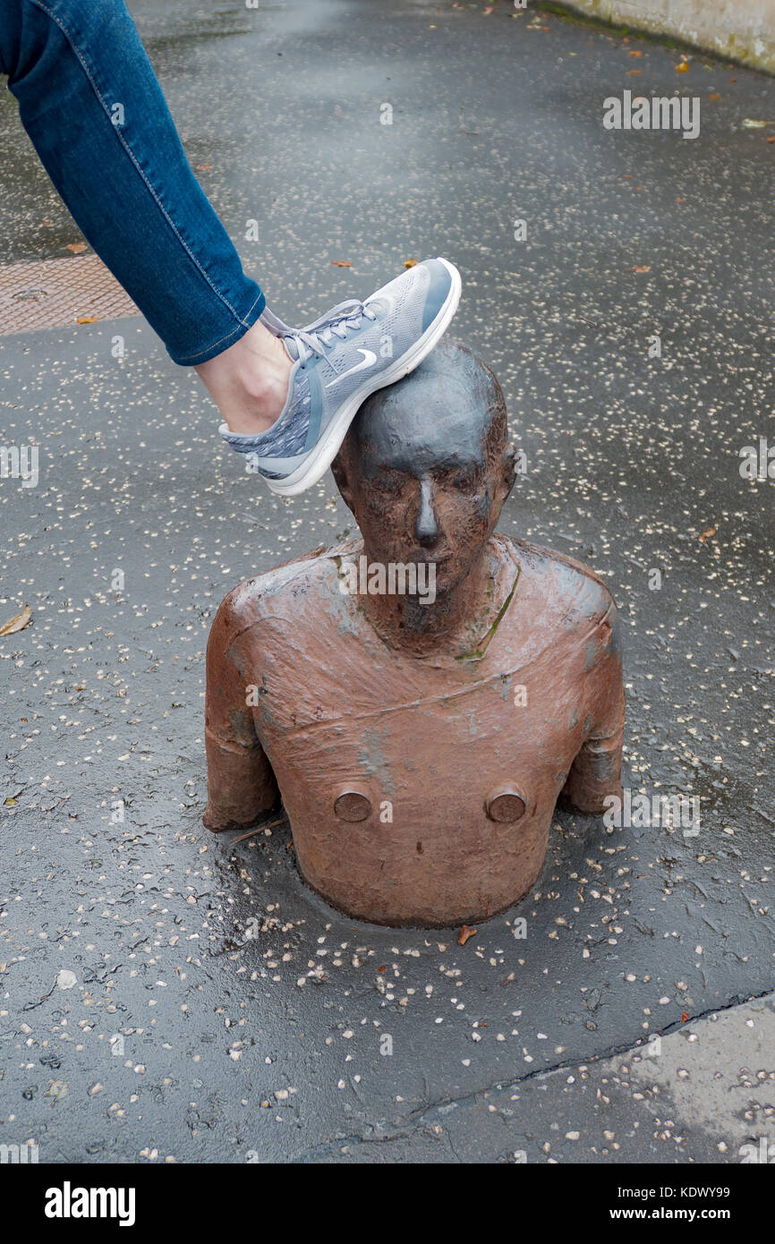 Una donna mette il piede sulla testa di Anthony Gormley scultura Foto Stock
