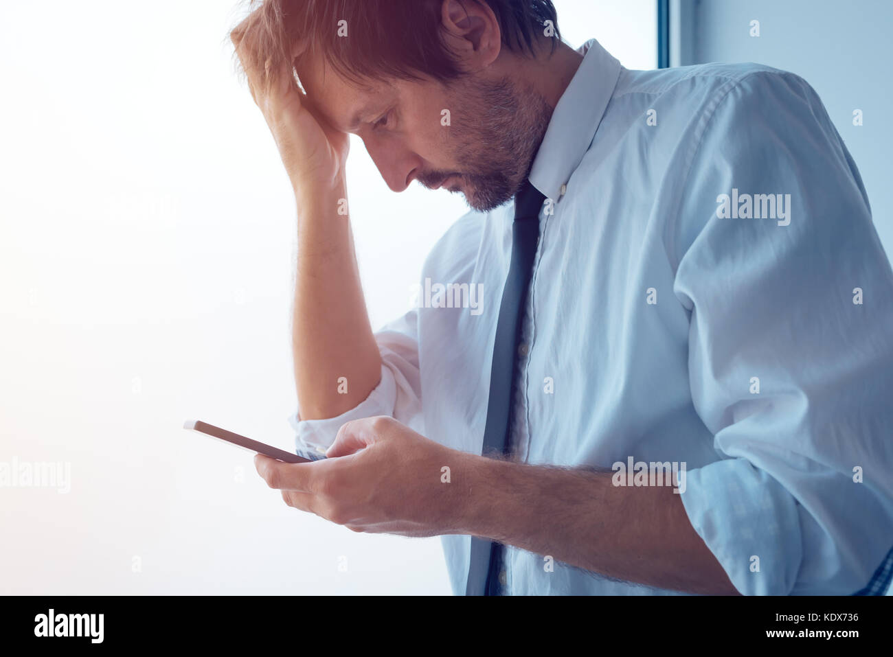 Imprenditore in piedi accanto alla finestra di ufficio e utilizza lo smartphone. business comunicazione tramite messaggi sms o mobile apps. persona d'affari ricevuto cattive Foto Stock