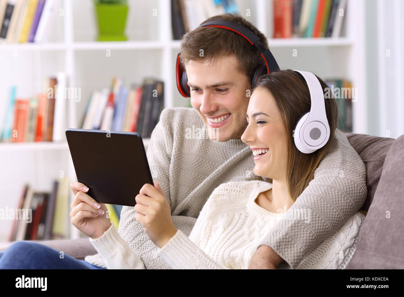 Coppia felice la visione di contenuti multimediali in linea in un tablet seduto su un divano a casa Foto Stock