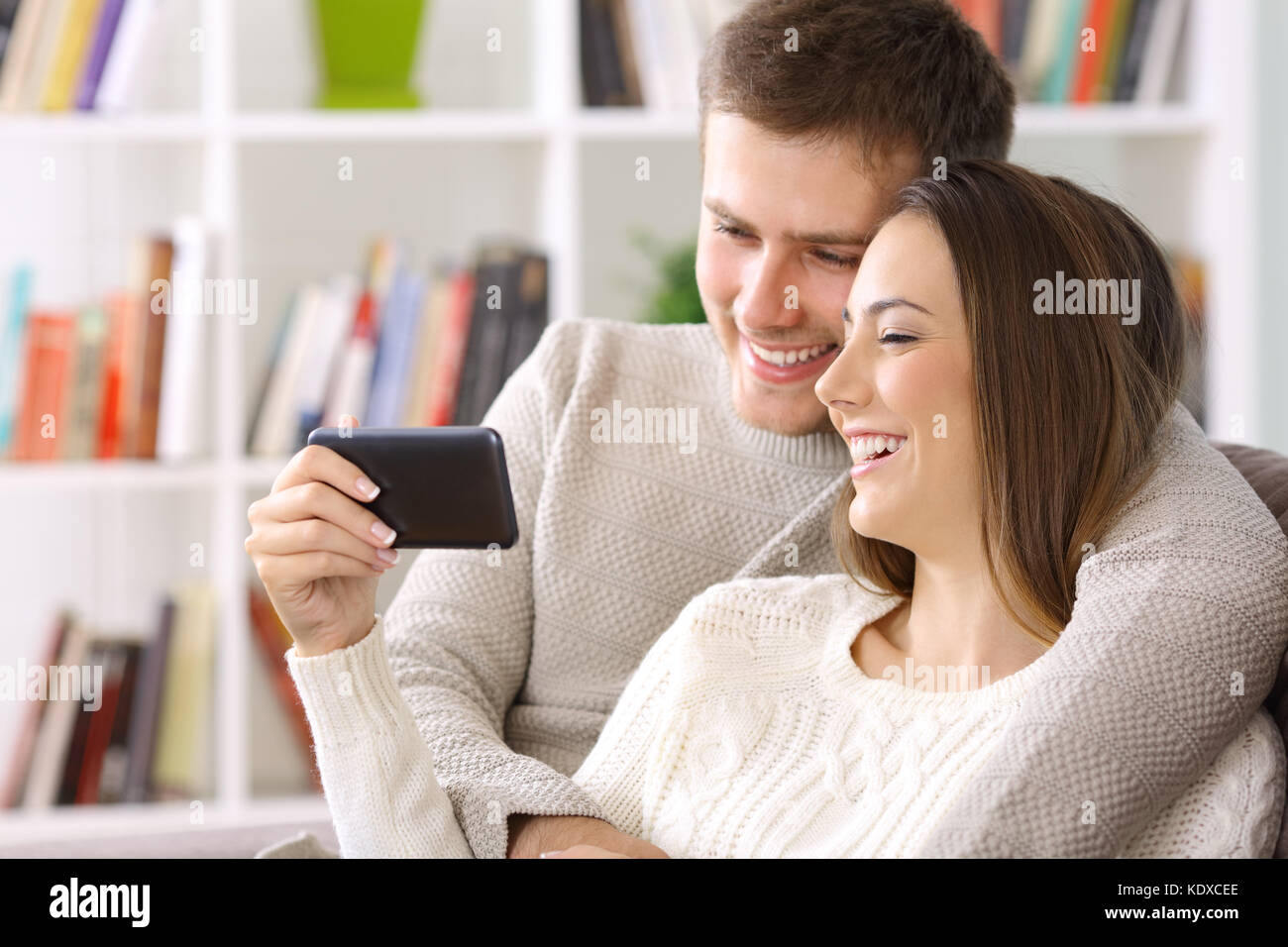 Coppia felice guardare on line il contenuto in uno smart phone seduto su un divano a casa Foto Stock