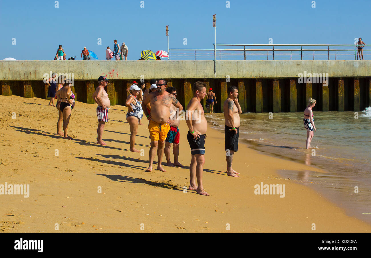Un gruppo di uomini e donne con grandi ventagli si affaccia sul mare dalla spiaggia della città vecchia di Albufera in Portogallo Foto Stock