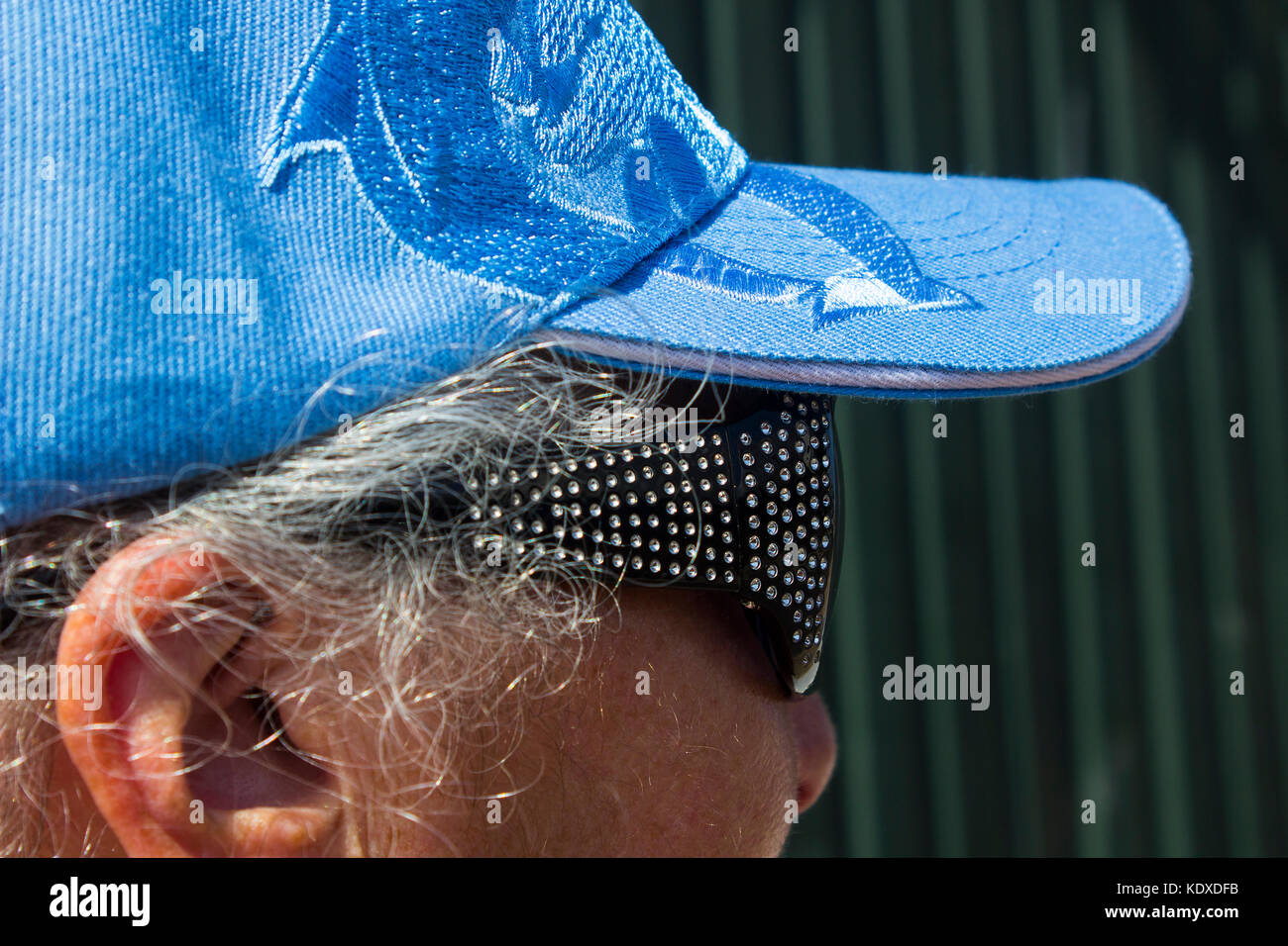 Primo piano della testa di una donna matura con capelli grigi che indossano un cappuccio di baseball con peci e occhiali da sole con cornice scura Foto Stock