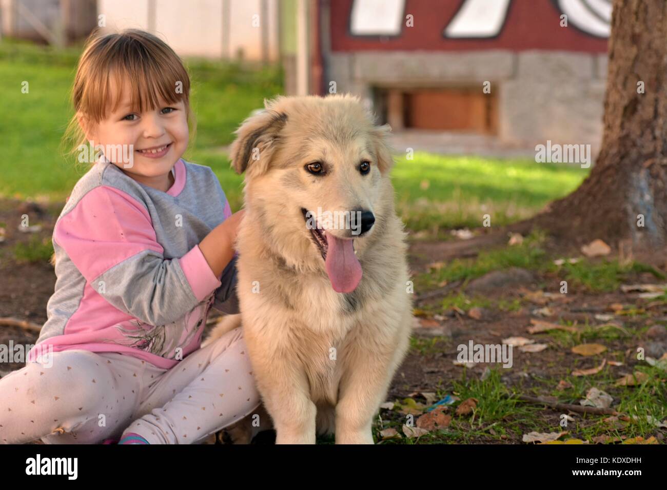 Ritratto di una giovane ragazza bionda bambino coccole cucciolo bianco all'aperto nel parco Foto Stock