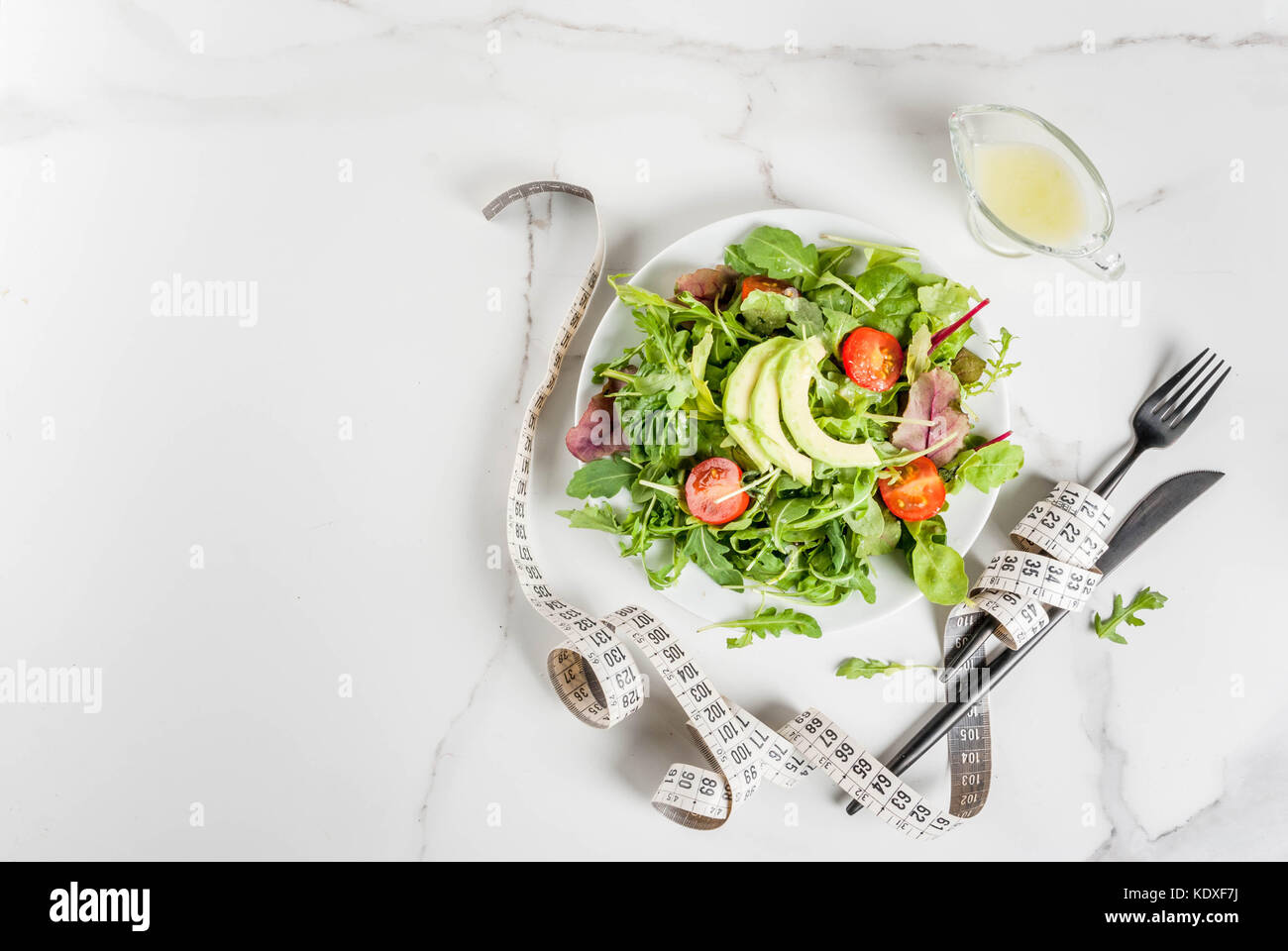 Una sana dieta bilanciata concetto, perdita di peso, il conteggio delle calorie. piastra con insalata verde foglie, pomodori e avocado con dressing di yogurt bianco, tabella, con Foto Stock