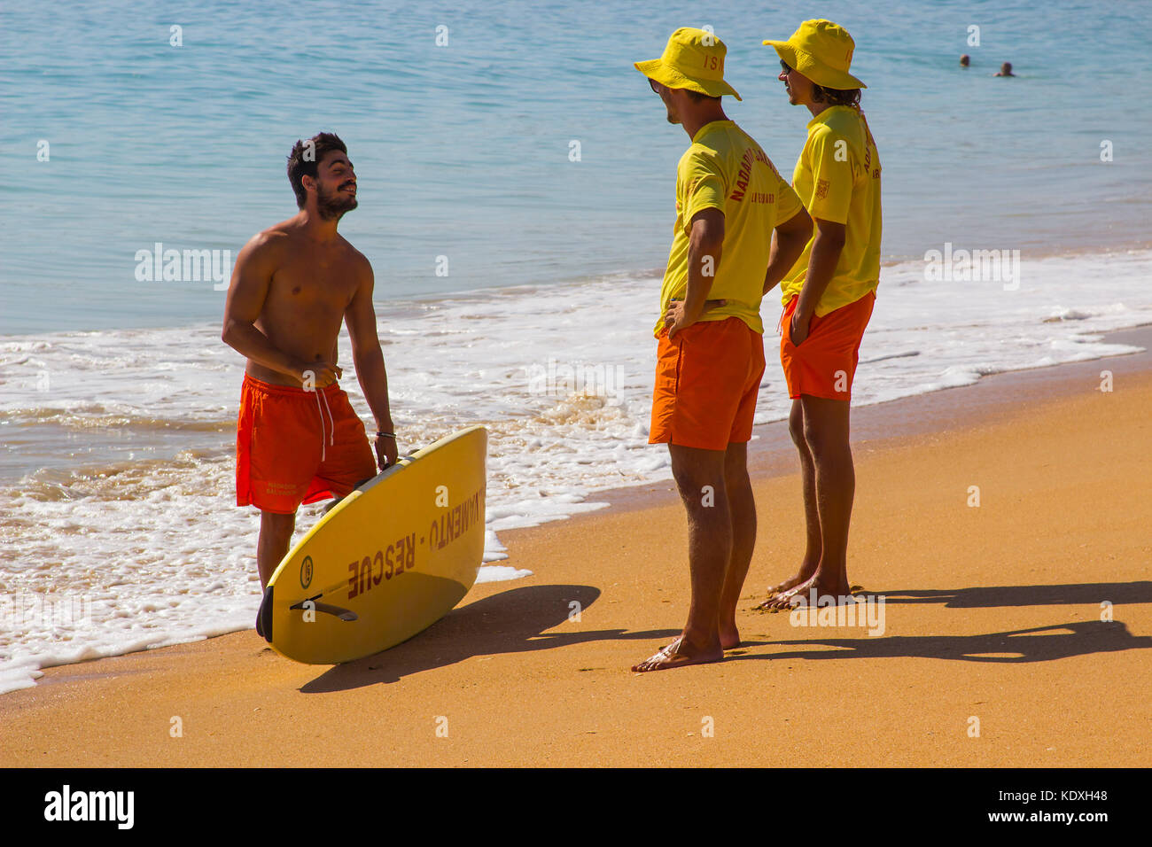 Due giovani bagnini chiacchierano con un surfista al bordo delle acque sulla spiaggia di Albfueria in Portogallo Foto Stock
