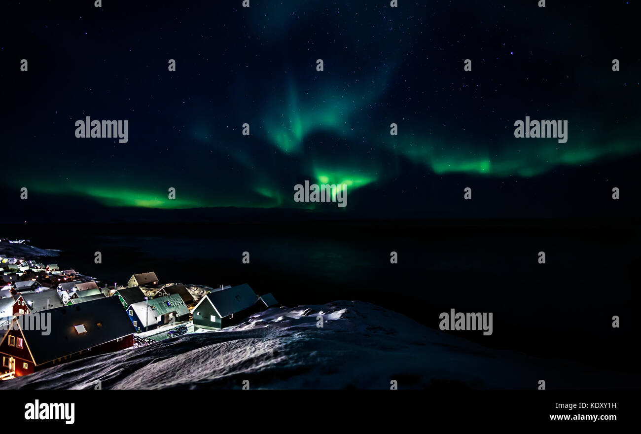 Incandescente verde dell'aurora boreale con stelle brillanti sul fiordo e villaggio inuit capanne, Nuuk, Groenlandia Foto Stock