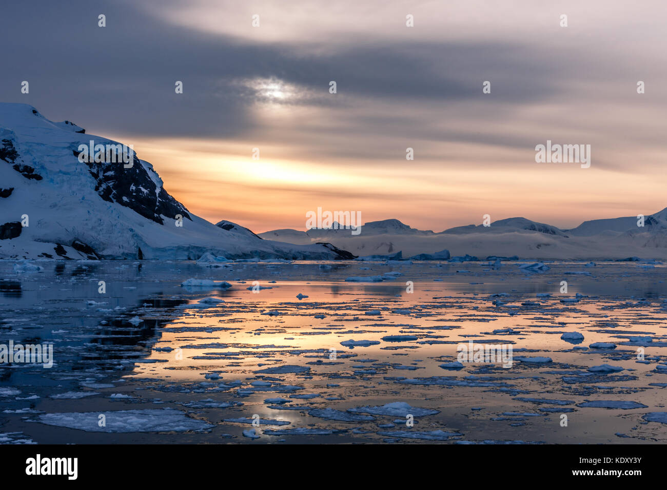 Arancione tramonto polari oltre le montagne con ghiacciai e drifting icebergs fuso a stretto di lemaire, Antartide Foto Stock